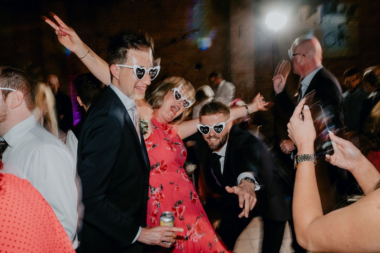 A blurred action image of guests posing for a photo being taken on someone's phone - all wearing the personalised sunglasses on the dancefloor. Photo by Matt Fox Photography. 