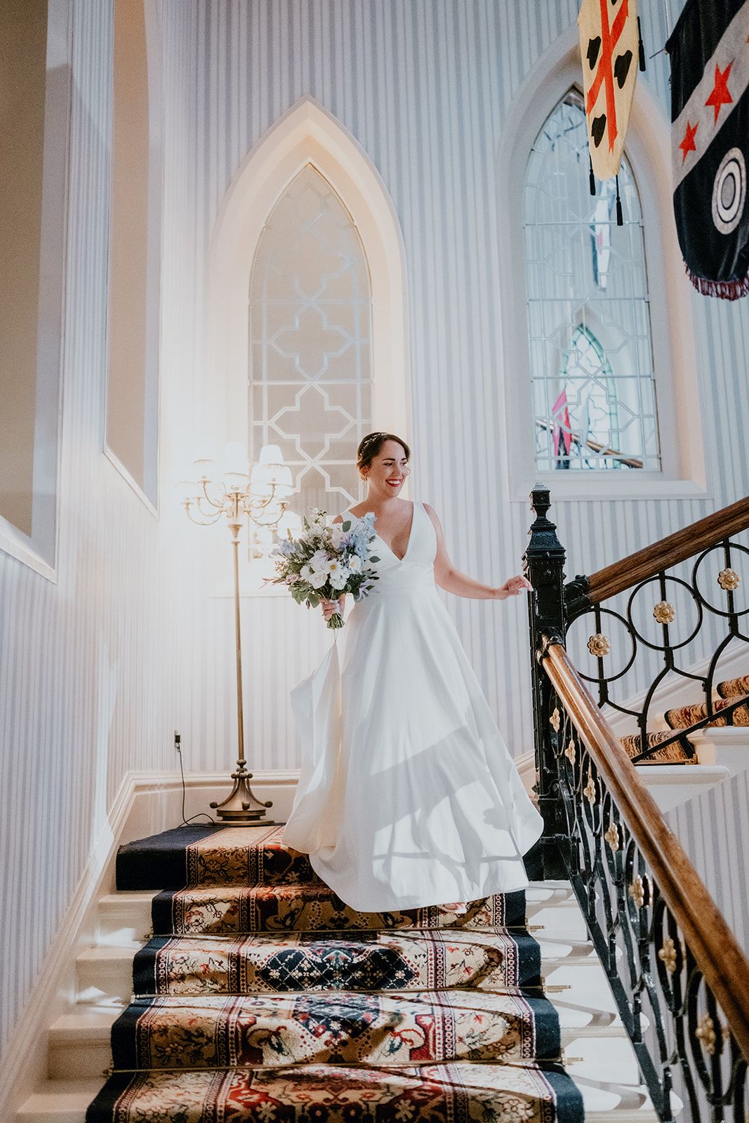 Adrianna walking down the stairs in her white wedding dress holding a bouquet at The Randolph Hotel in Oxford. Photo thanks to Matt Fox Photography.