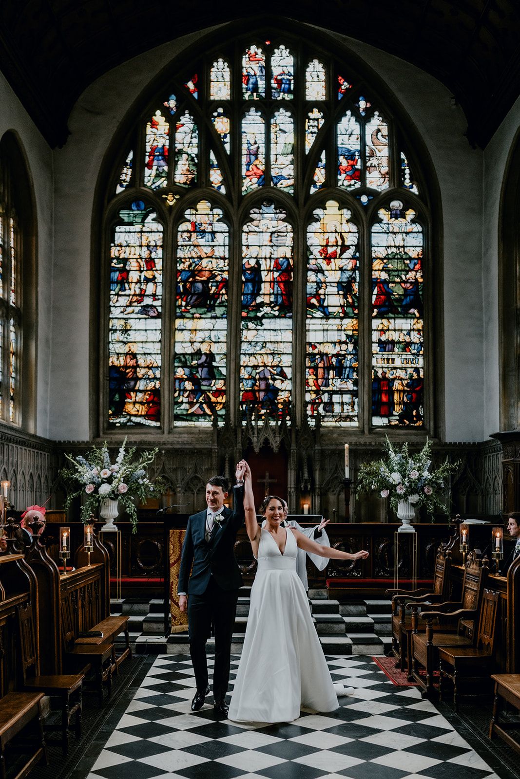 Adrianna and James holding hands raised in the air to celebrate being newlyweds as they exit down the aisle of Wadham College Chapel. Photo thanks to Matt Fox Photography.