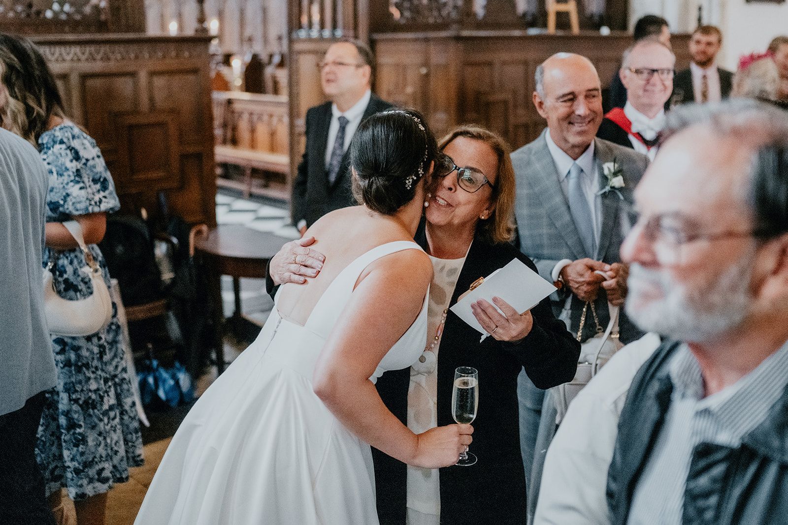 Adrianna holding a glass of prosecco greeting one of her family in an embrace after their wedding ceremony. Other family members look on in the background. Photo thanks to Matt Fox Photography.