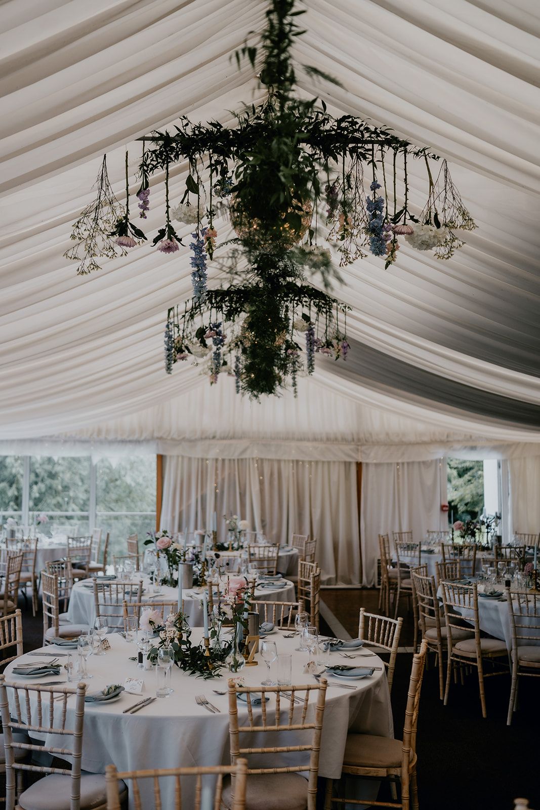 A tall view of the inside of the marquee with the tables, place settings, flower arrangements and chairs. A large flower chandelier hangs from the ceiling of the marquee at Cherwell Boathouse. Photo courtesy of Matt Fox Photography.