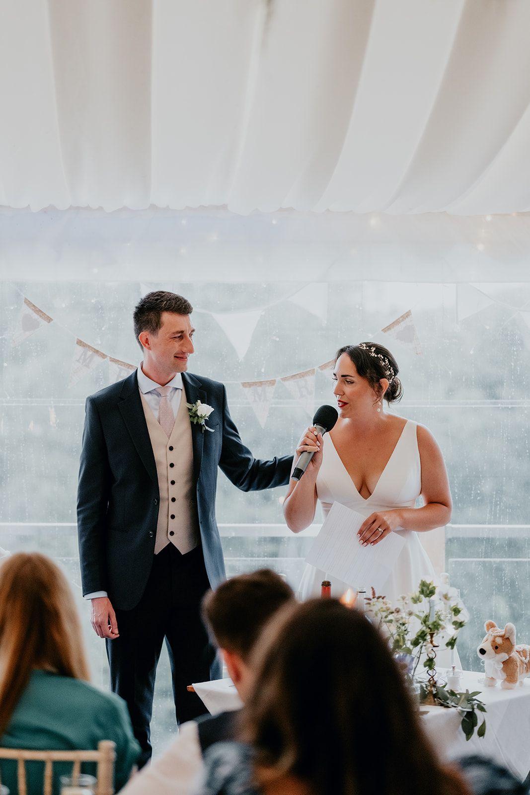 James smiling at Adrianna with his hand on her shoulder as she makes a speech in the marquee. Guests watch on in the foreground. Photo courtesy of Matt Fox Photography.