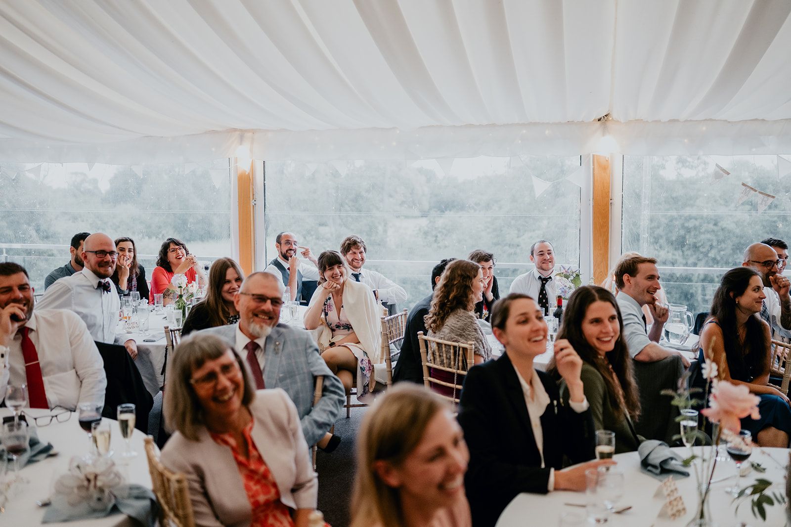 Guests watch the video as part of the wedding speeches, all laughing and smiling in the marquee at Cherwell Boathouse. Photo courtesy of Matt Fox Photography.