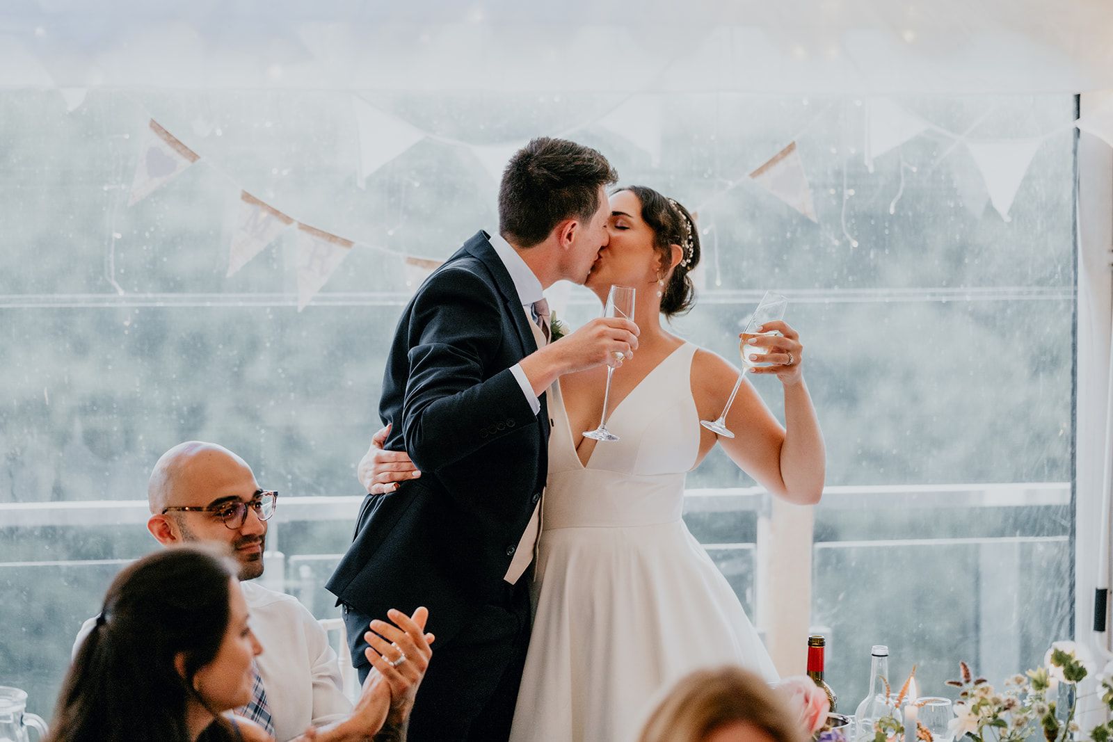 Adrianna and James kiss and toast with prosecco at the end of their wedding speeches in the marquee at Cherwell Boathouse. Photo courtesy of Matt Fox Photography.